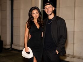Kennedy Alexa wearing a black dress posing elegantly next to her partner, footballer James Maddison, in a matching black outfit and cap.
