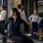 Práctica de Yoga Estilismo Laboral, Diverse professionals practicing mindful breathing and gentle desk yoga in a modern corporate office setting.